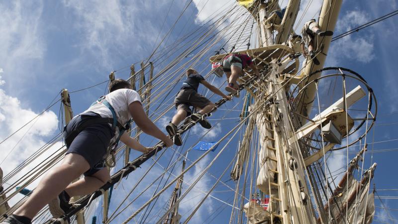 Deltakere klatrer i riggen på et seilskip under Tall Ships Races.