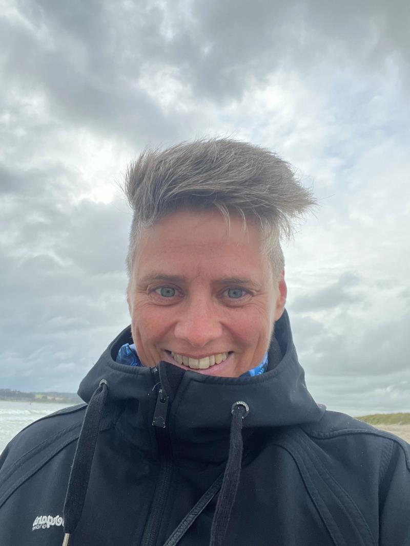 Portrett av en person utendørs, iført mørk ytterjakke, med naturlig bakgrunn og overskyet himmel.