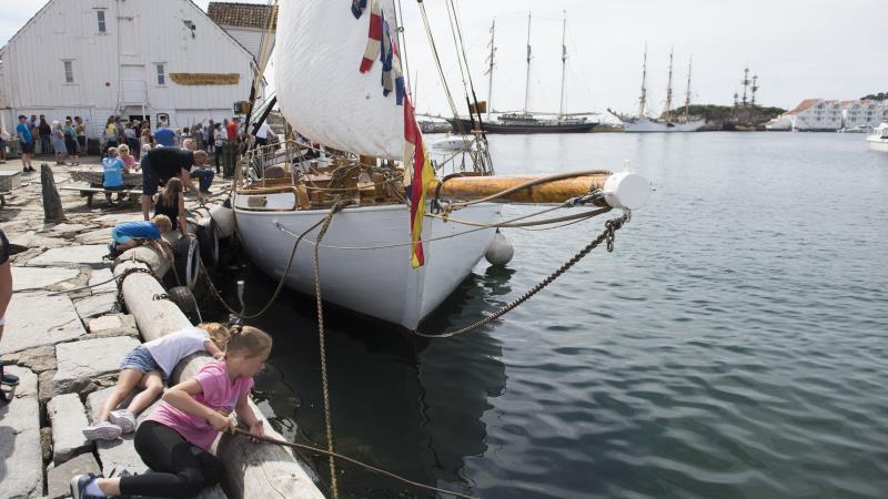 Bilde av en skute i havnen i Tananger og barn som fisker.