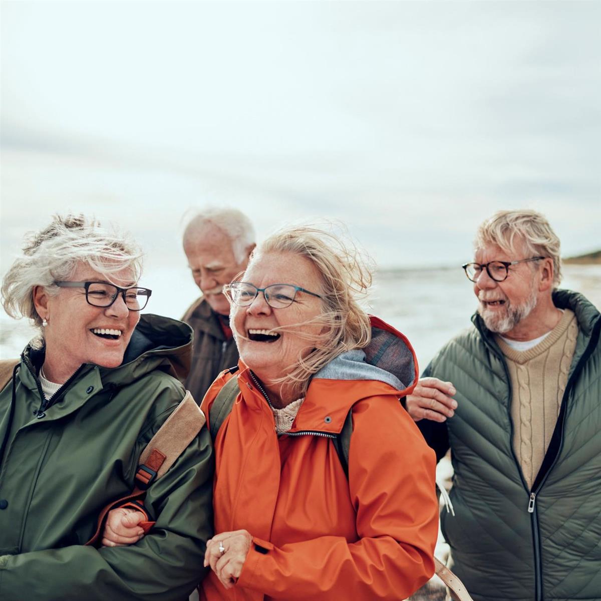 Bildet viser glade kvinner og menn på tur langs stranden. - Klikk for stort bilde