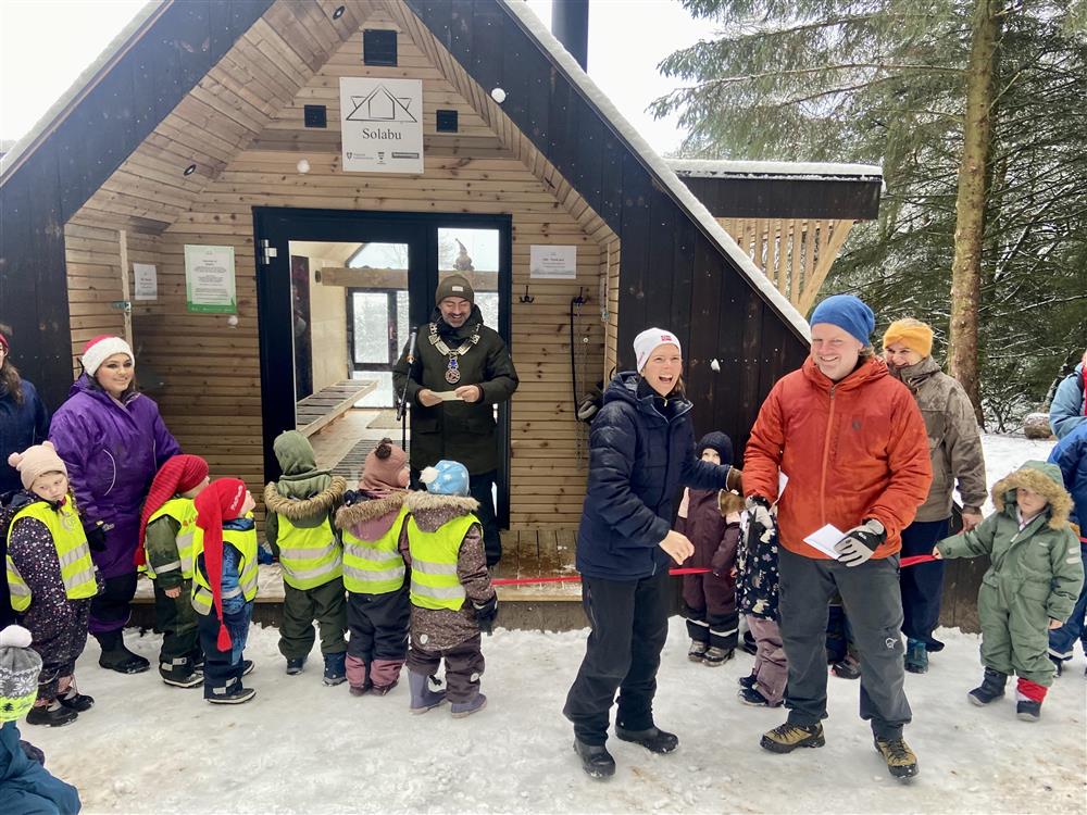 Foto av ordføreren som står foran dagsturhytta. Vinnerne av navnekonkurransen mottar gavekort. - Klikk for stort bilde