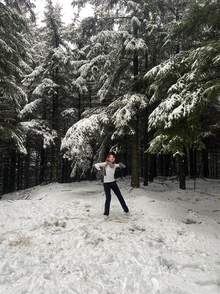 Foto av ung jente med ørevarmere som danser blant snøkledde trær i skogen.  - Klikk for stort bilde