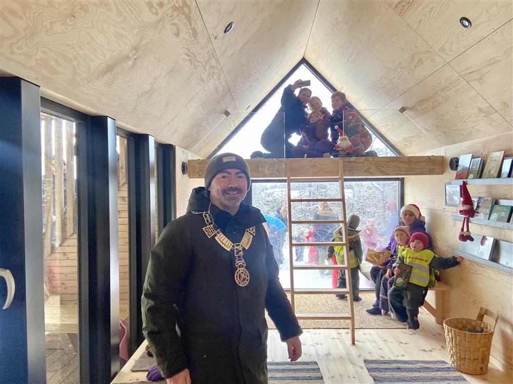 Foto fra innsiden av hytta. Ordfører Tom Henning Slethei smiler. Barn på hemsen i bakgrunnen.  - Klikk for stort bilde