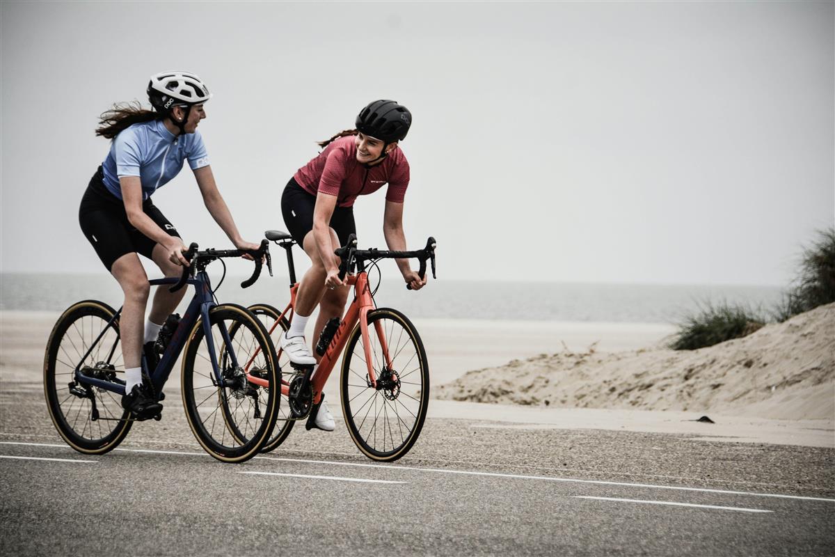 To kvinnelige syklister som sykler på veien langs en strand.  - Klikk for stort bilde